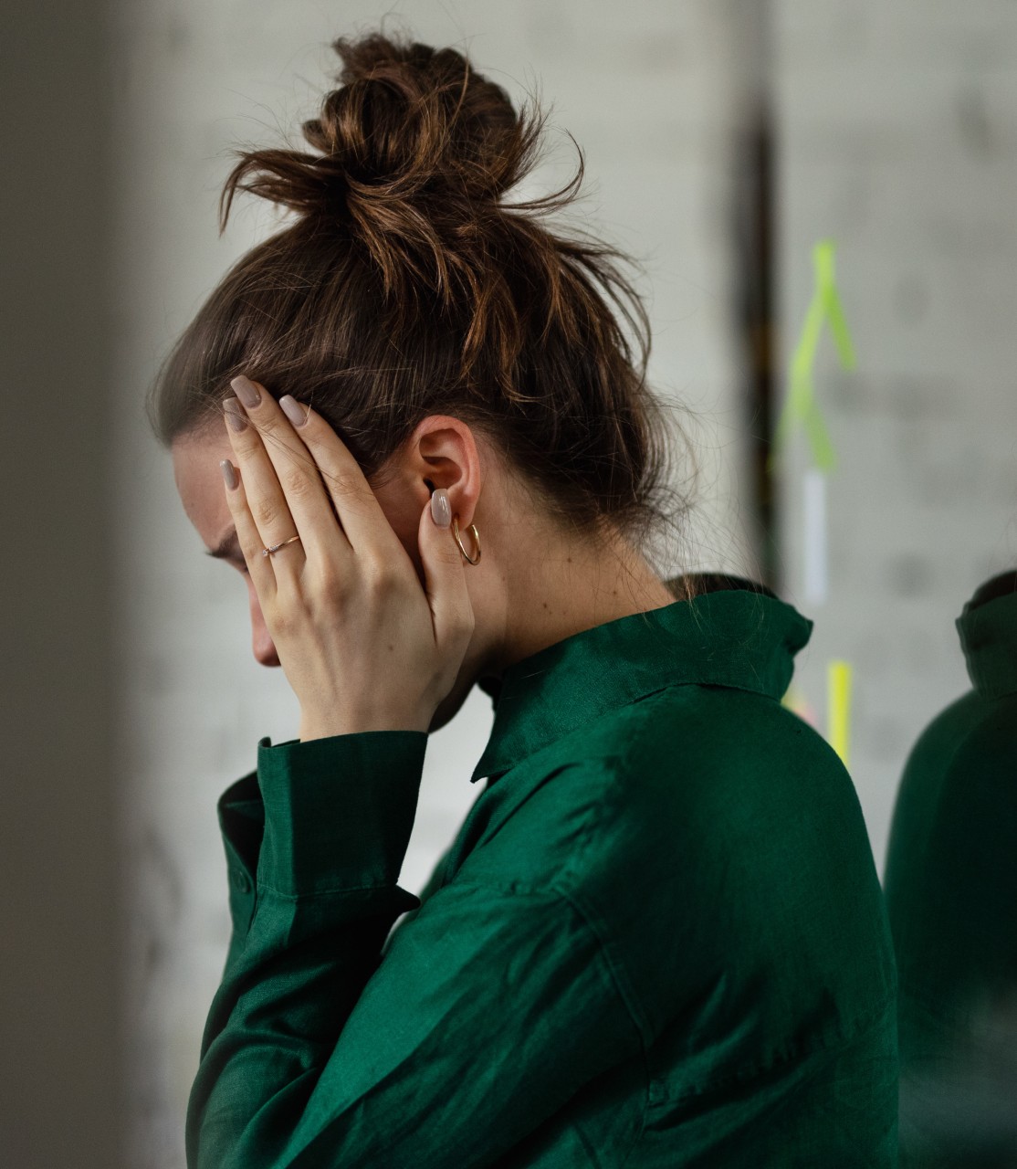 A woman leans against a wall, with her hands framing her face. She appears to be overwhelmed or stressed.