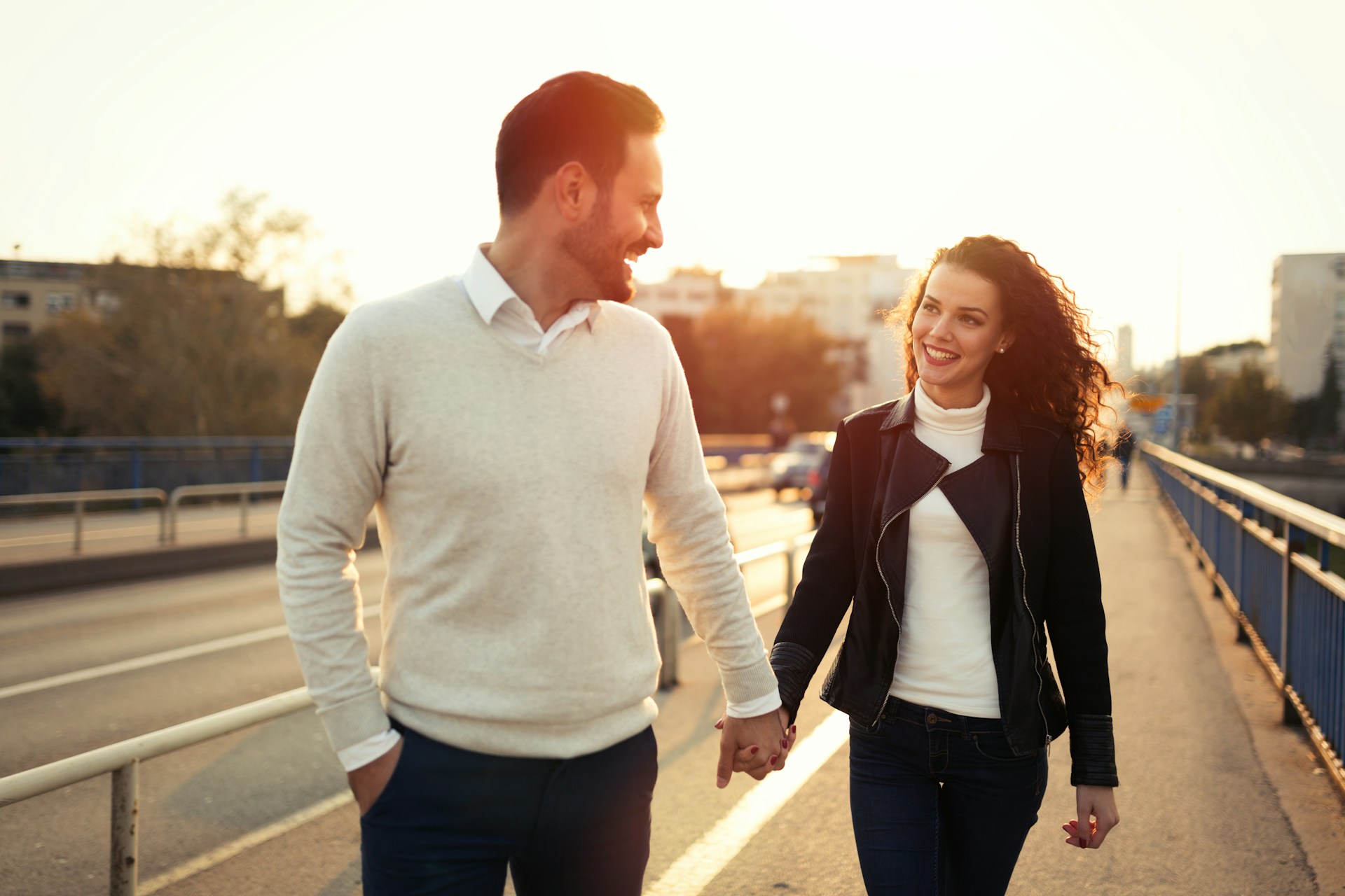 A man smiling is walking, while holding hands with a woman.